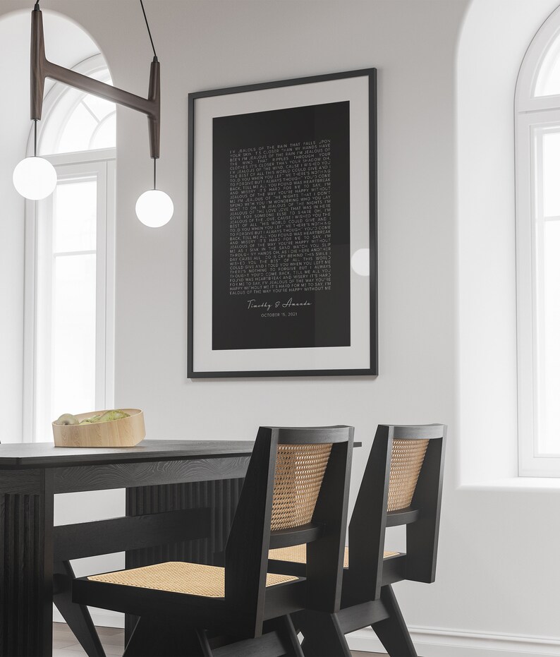 May include: Black and white framed print with a poem about love and a couple's names and wedding date. The print is hanging on a white wall above a black dining table with two black chairs.