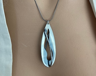 Puede incluir: Un collar de plata con un colgante abstracto único. El colgante tiene forma de lágrima con un diseño recortado.