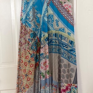 Puede incluir: Un vestido largo sin mangas con un dise&ntilde;o de patchwork. El vestido presenta una variedad de estampados, incluyendo estampados florales, paisley y geom&eacute;tricos en tonos de azul, rosa y beige. El vestido est&aacute; colgado en una percha blanca.