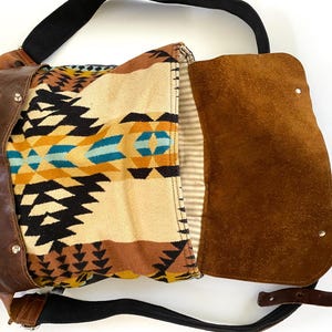 May include: A brown leather messenger bag with a flap closure. The bag features a patterned fabric interior with black, yellow, and turquoise geometric designs. It has a black shoulder strap and a brown leather exterior.