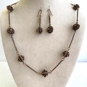 Può includere: Un set di gioielli color rame composto da una collana e un paio di orecchini pendenti. La collana presenta una catena delicata intervallata da perline rotonde in stile filigrana. Gli orecchini abbinati riprendono il design con ganci.