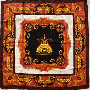 Puede incluir: Pañuelo cuadrado de seda con un diseño ornamental detallado. El pañuelo presenta un centro negro con un borde decorativo dorado y rojo. El borde exterior es marrón oscuro. El pañuelo tiene una estética vintage.