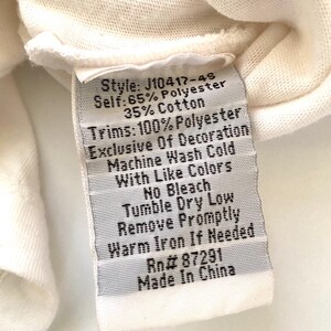May include: Close-up of a white clothing tag with black text. The tag lists the style, fabric composition (65% polyester, 35% cotton), and care instructions, including machine wash cold and tumble dry low. The tag also states "Made in China."