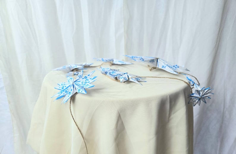 May include: A string of blue and white origami stars hanging from a table covered in a white tablecloth. The stars are connected by twine.