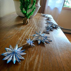 May include: A string of blue and white paper stars with a blue polka dot pattern, strung together with twine. The stars are hanging on a wooden surface.