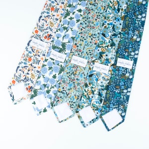 Pode incluir: Cinco gravatas dispostas lado a lado, cada uma com um padr&atilde;o floral distinto em tons de azul, branco e laranja. Cada gravata inclui uma etiqueta retangular branca com o texto Hayden Harlow USA costurado na superf&iacute;cie do tecido.