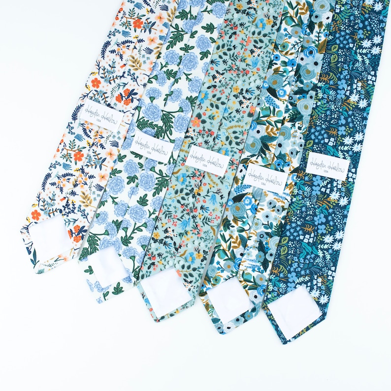 Pode incluir: Cinco gravatas dispostas lado a lado, cada uma com um padr&atilde;o floral distinto em tons de azul, branco e laranja. Cada gravata inclui uma etiqueta retangular branca com o texto Hayden Harlow USA costurado na superf&iacute;cie do tecido.