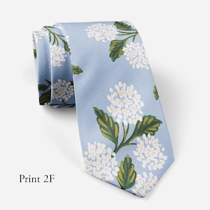 Può includere: Cravatta azzurra con motivo floreale. La cravatta presenta grappoli di fiori bianchi con foglie verdi. Il testo "Print 2F" è stampato in basso a sinistra.