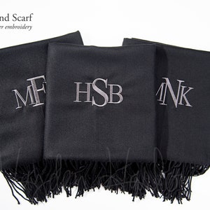 Könnte beinhalten: Drei schwarze Schals aus Wollmischung mit silbernen Stickinitialen. Die Initialen sind "MF", "HSB" und "NK".