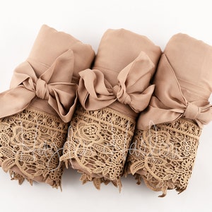 Peut inclure: Trois robes en satin marron avec des bordures en dentelle, nouées avec des nœuds en satin assortis. Les robes sont enroulées et disposées en rangée.