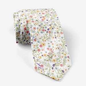 May include: A white tie with a floral design. The tie is patterned with small flowers in pink, yellow, purple, and blue, with green leaves and stems. The tie is folded and displayed against a white backdrop.