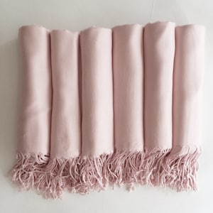 Peut inclure: Collection de six écharpes rose pâle roulées, avec des bords frangés. Les écharpes sont disposées en rang, mettant en valeur leur texture douce et leur couleur. Les franges ajoutent un élément décoratif.