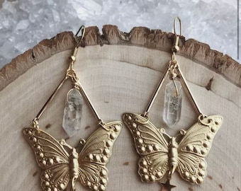 Puede incluir: Pendientes de mariposa dorados con detalles de cristal transparente y un dije de estrella. Los pendientes cuelgan de un marco de alambre geométrico.