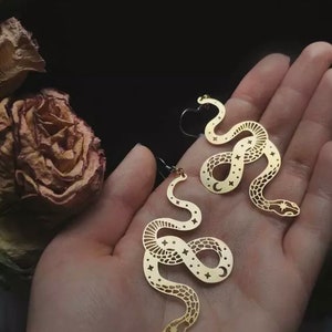 May include: A pair of gold-tone earrings featuring a snake design with a crescent moon and stars cutouts.