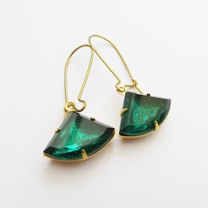 May include: Gold-coloured earrings featuring emerald green, fan-shaped pendants. The earrings have a hook closure. The pendants are faceted and set in gold. The background is white.