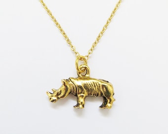 May include: A gold-colored necklace featuring a rhino pendant. The rhino pendant is detailed with textured skin and a small horn. The chain is delicate and gold, creating a simple yet eye-catching piece of jewelry.