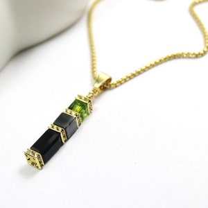 May include: A gold chain necklace with a pendant featuring a vertical row of black and green square-shaped stones.