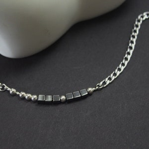 Puede incluir: Un collar de cadena de plata con una fila de cuentas cuadradas negras y cuentas redondas plateadas.