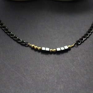 May include: A black chain necklace with a row of black square beads and gold round beads.