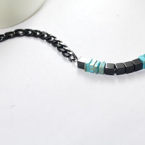 Puede incluir: Un collar de cadena negra con una fila de cuentas cuadradas de color turquesa y negro.