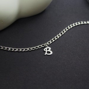Puede incluir: Un brazalete de cadena de plata con un dije de plata en forma de la letra B.