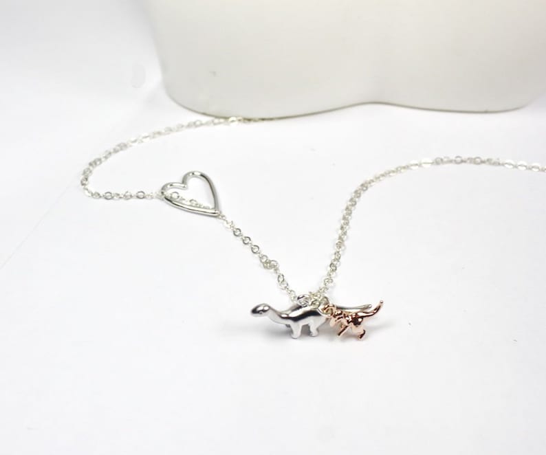 May include: A silver necklace with a heart charm and two dinosaur charms, one silver and one rose gold.