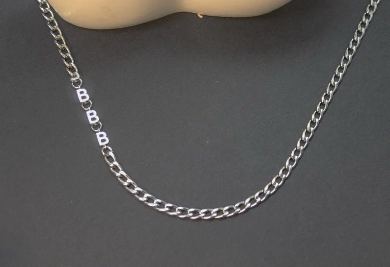 May include: A silver chain necklace with a series of letter 'B' charms.
