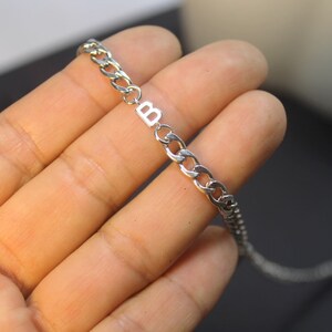 May include: A silver chain necklace with a silver charm that has the letter "B" on it.