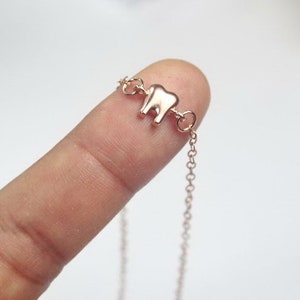 May include: A delicate rose gold necklace with a small tooth charm. The chain is thin and delicate, and the tooth charm is simple and elegant.