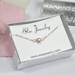 May include: A silver jewelry box with a white card inside. The card has the text "Else Jewelry" and the website address "www.elsejewelry.com". A delicate gold chain necklace with a small tooth charm is displayed on the card.