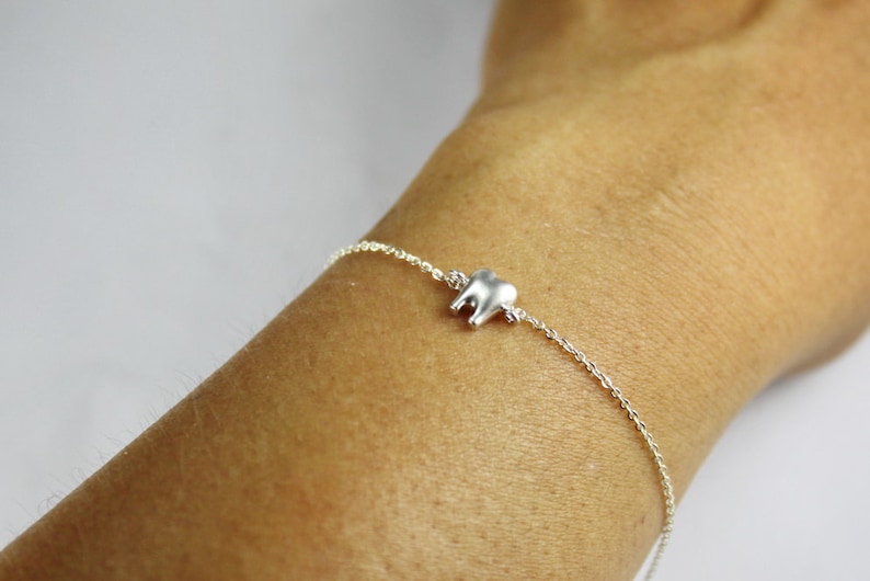 May include: A silver chain bracelet with a small silver tooth charm.