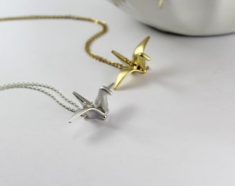 Könnte beinhalten: Zwei zarte Halsketten mit Origami-Kranich-Anhängern. Eine Halskette hat einen goldenen Kranich-Anhänger, die andere einen silbernen Kranich-Anhänger.