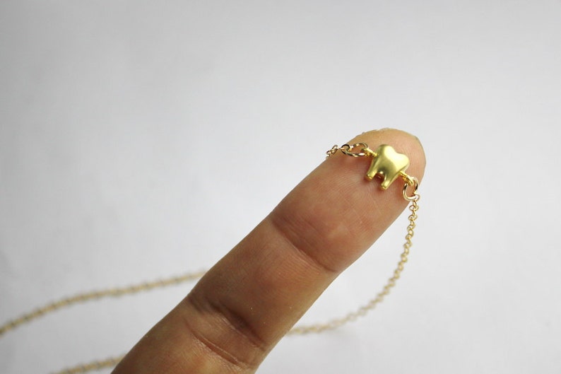 May include: A gold chain necklace with a small gold tooth charm.