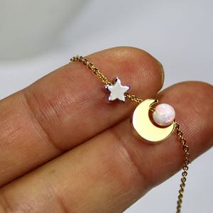 May include: A gold chain necklace with a crescent moon charm and a star charm. The moon charm has a white opal stone in the center.