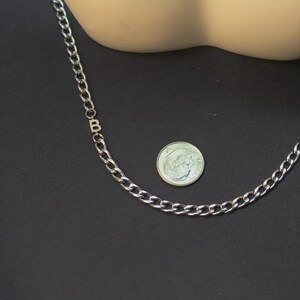 May include: A silver chain necklace with a letter 'B' charm. The chain is about the size of a dime.