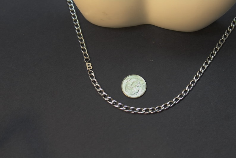 May include: A silver chain necklace with a letter 'B' charm. The chain is about the size of a dime.