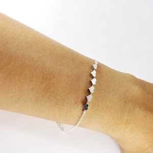 Pode incluir: Um bracelete de corrente de prata com uma fila de pequenos pingentes em forma de coração.