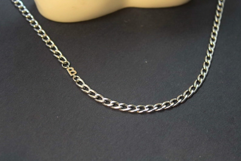 May include: A silver chain necklace with a small gold letter 'B' charm.