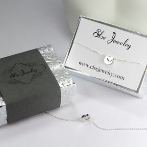 May include: A silver necklace with a small circle pendant featuring a heart cutout. The necklace is displayed in a silver box with a black label that reads "Else Jewelry" and a white card with the text "Else Jewelry" and "www.elsejewelry.com".