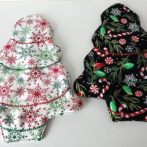 May include: Two Christmas tree-shaped cloth pads. One is white with red and green snowflakes. The other is black with candy canes, lights, and snowflakes. Both have a decorative stitched border.