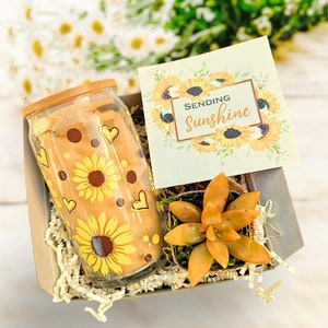 May include: A gift box filled with a glass tumbler with a sunflower design, a small succulent plant, and a card that says "Sending Sunshine".