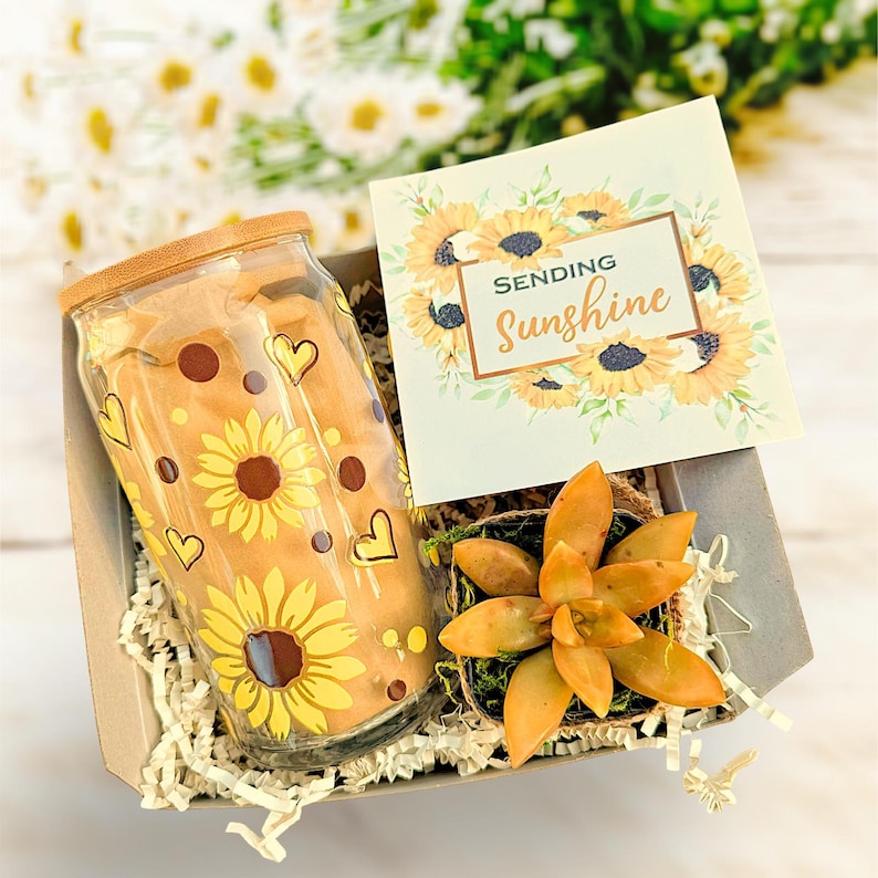 May include: A gift box filled with a glass tumbler with a sunflower design, a small succulent plant, and a card that says "Sending Sunshine".