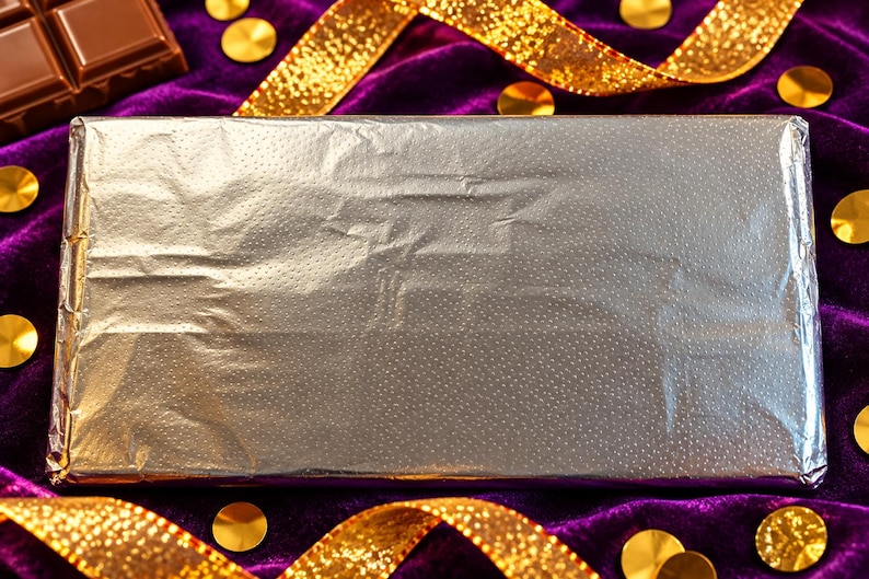 May include: A rectangular chocolate bar wrapped in smooth, reflective silver foil. The metallic packaging has a subtle, fine-textured surface pattern and is positioned horizontally, centered in the frame.