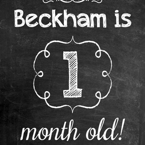 May include: A chalkboard-style sign with white lettering that reads "Beckham is 1 month old!". The number 1 is inside a decorative frame. The background is black with white dots and swirls.