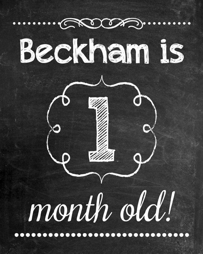 May include: A chalkboard-style sign with white lettering that reads "Beckham is 1 month old!". The number 1 is inside a decorative frame. The background is black with white dots and swirls.