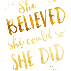 May include: A white background with gold text that reads "She BELIEVED she could so SHE DID." The text has a textured, metallic appearance with gold paint splatters. The words "Joyful Art Designs" are at the bottom.