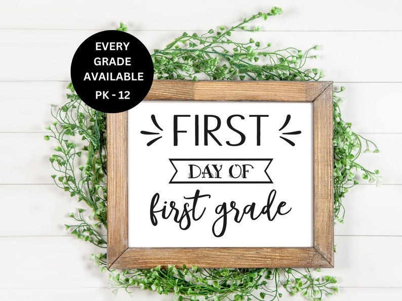 Pode incluir: Uma placa branca enquadrada com texto preto que diz "FIRST DAY OF first grade". A placa &eacute; cercada por galhos verdes frondosos.