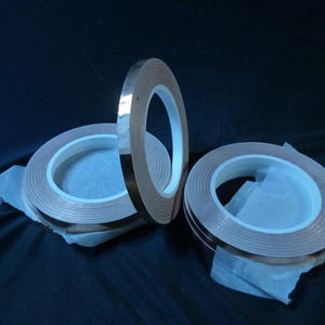 May include: Three rolls of copper tape, each with a brown adhesive backing and a shiny copper surface. The rolls are stacked on top of each other.