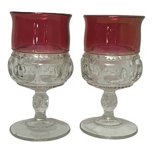 Könnte beinhalten: Zwei klare Weingläser mit rubinrotem Rand. Die Gläser haben ein strukturiertes, erhabenes Muster.