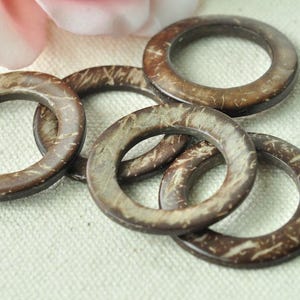 May include: Five brown coconut shell rings, each with a smooth, polished finish and a natural wood grain pattern. The rings are stacked on top of each other, creating a visually appealing display.